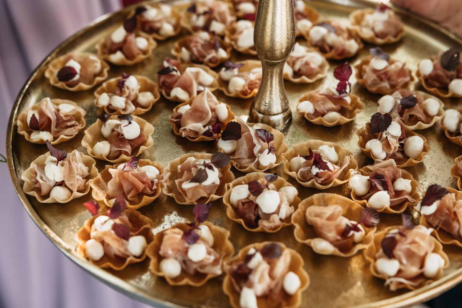 Close-up of elegant gold tray filled with decorative bite-sized appetizers topped with cream and dried fruits.