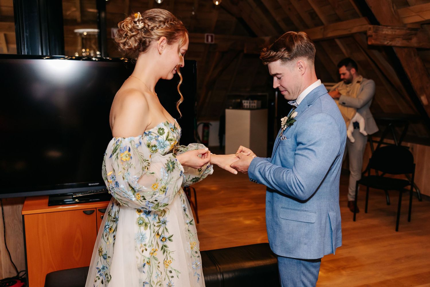 Bride and groom exchange wedding rings during intimate indoor ceremony in rustic barn venue.