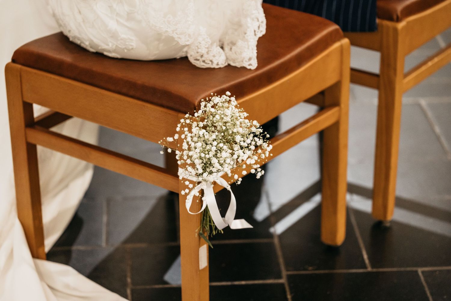 Small bouquet of baby's breath tied with ribbon decorating wooden church chair at wedding.