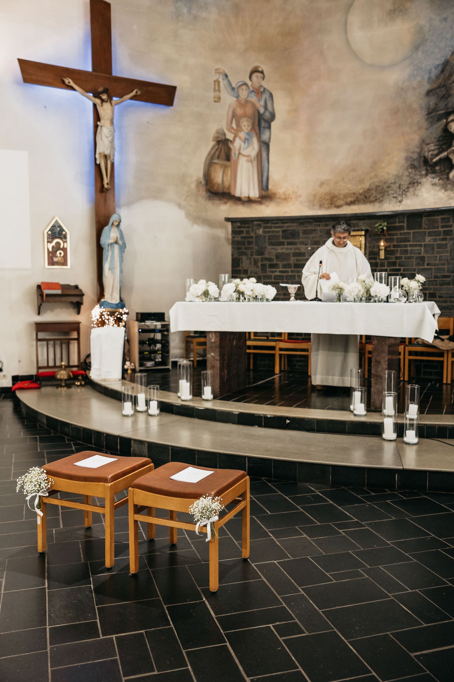 Catholic church altar decorated with white flowers and candles for a wedding ceremony with priest at the altar.