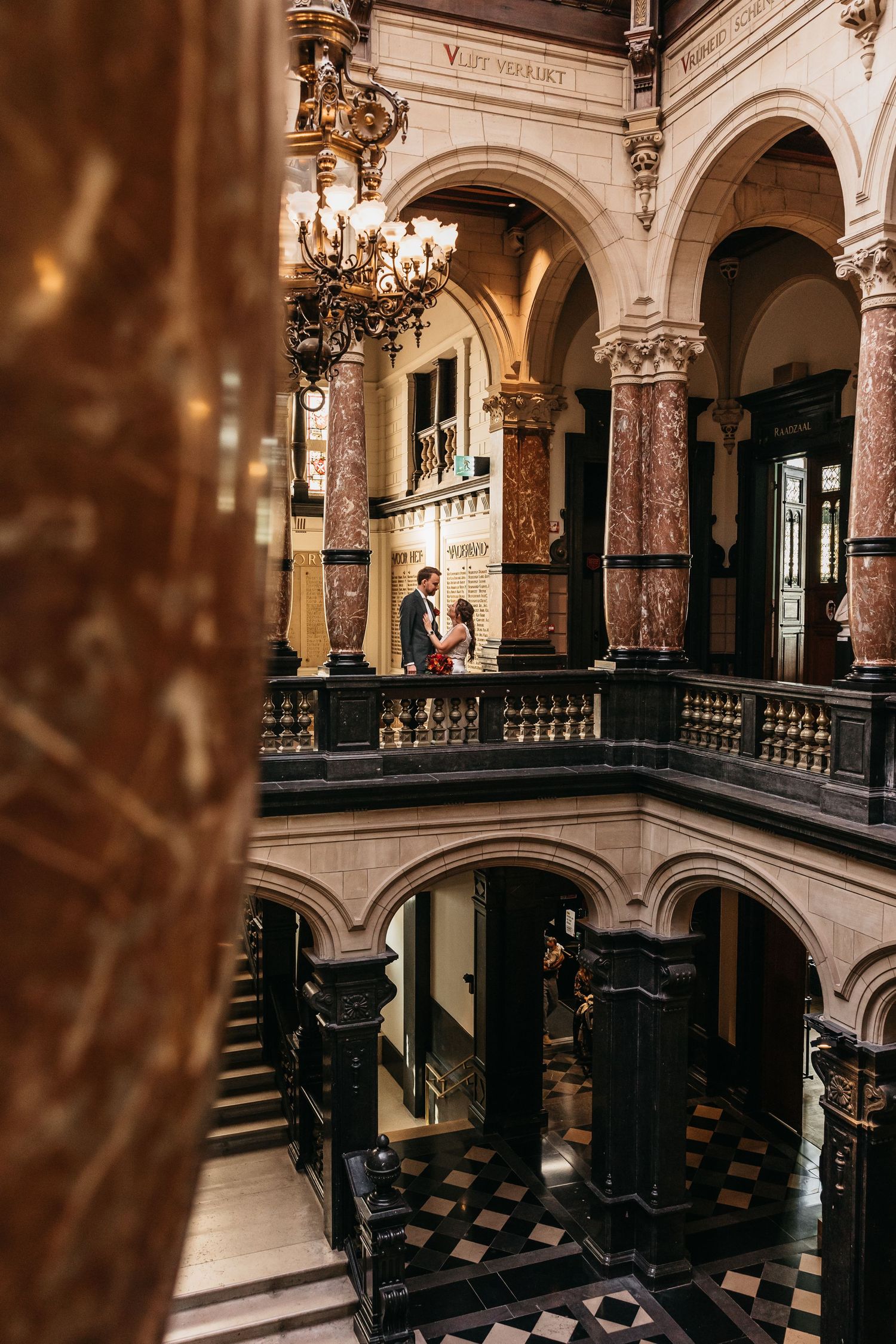 Bride and groom sharing a kiss on ornate balcony in historic building.