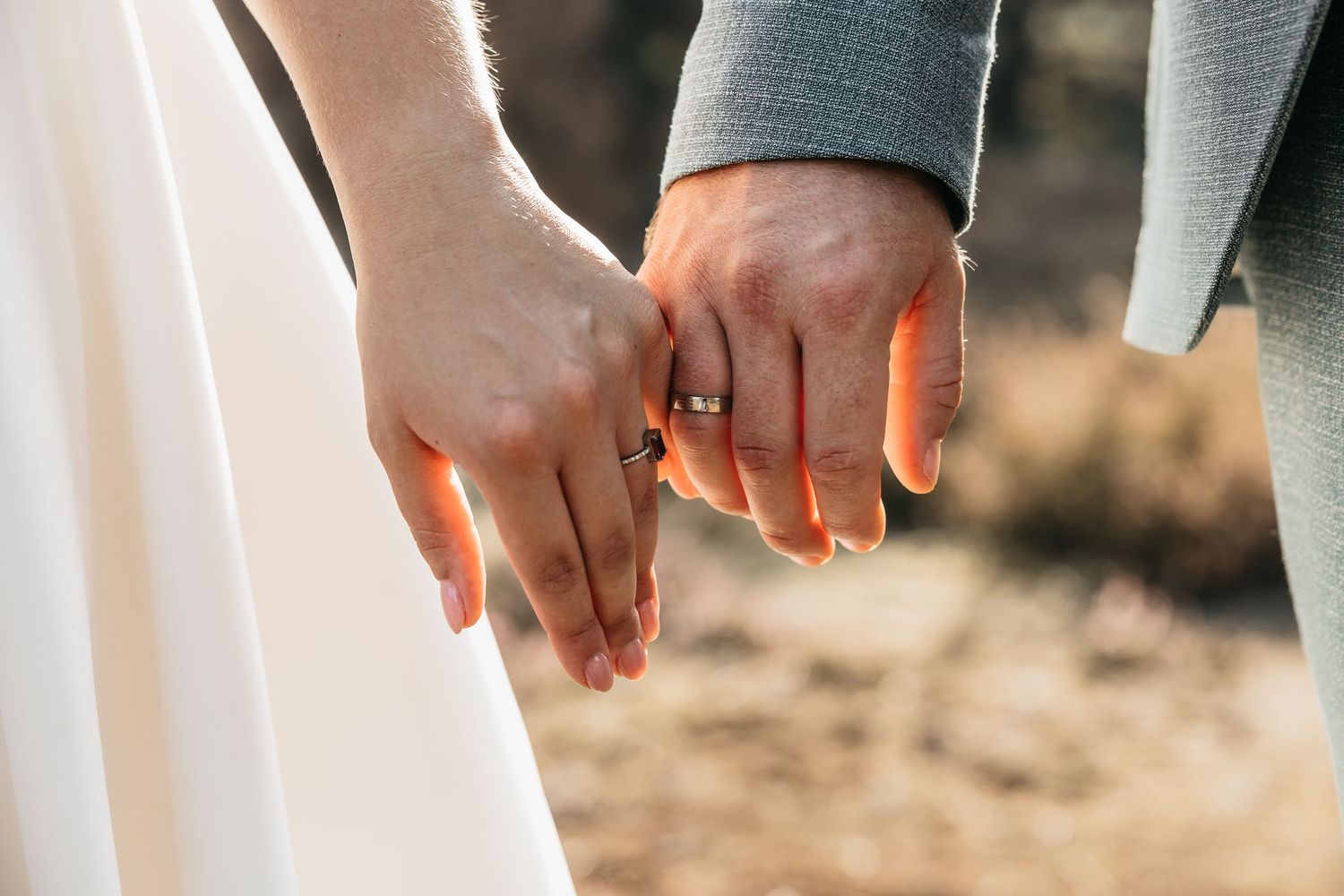 Close-up of bride and groom holding hands showing their wedding rings in warm golden light.