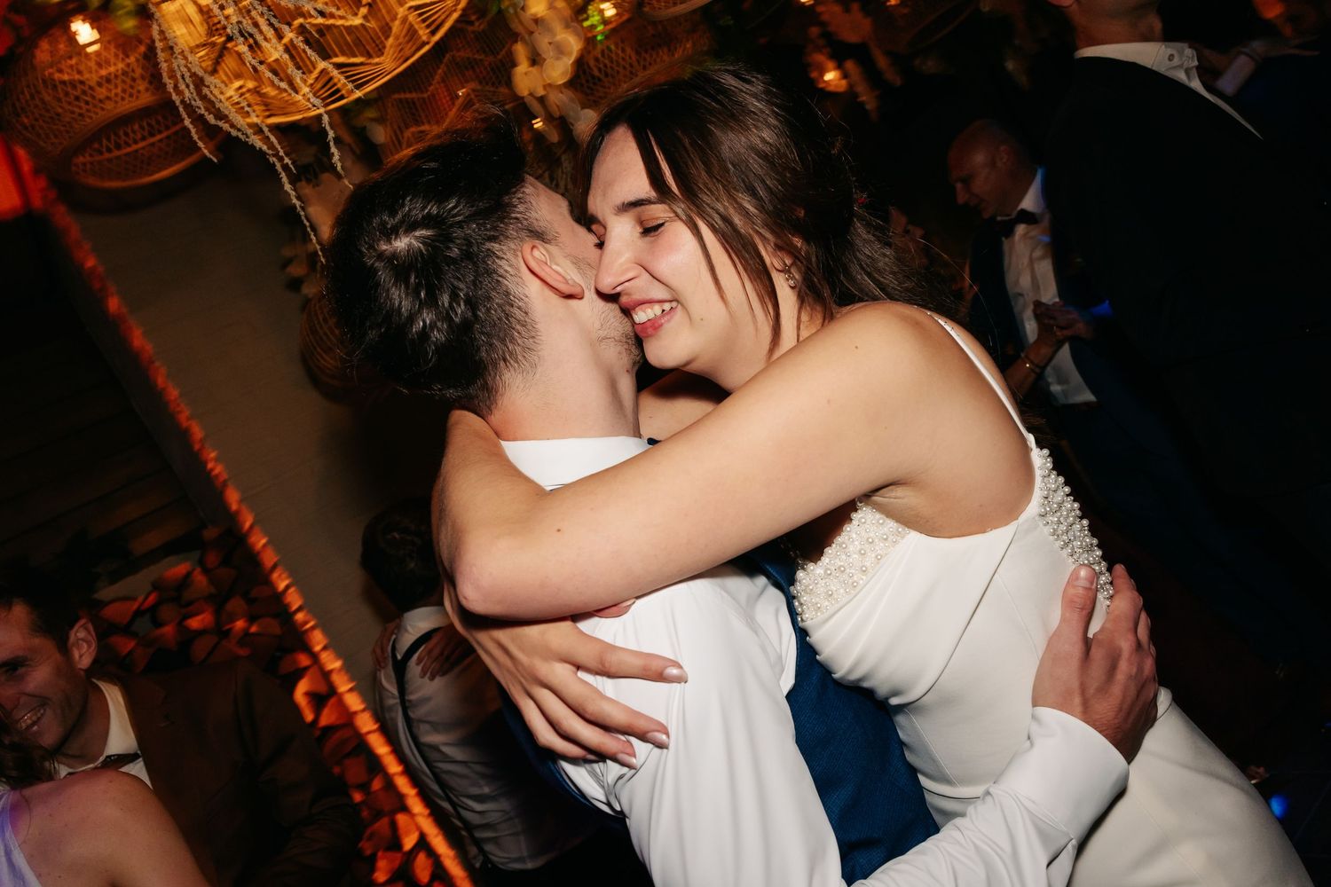 Bride hugging and kissing a guest joyfully during wedding reception celebrations.