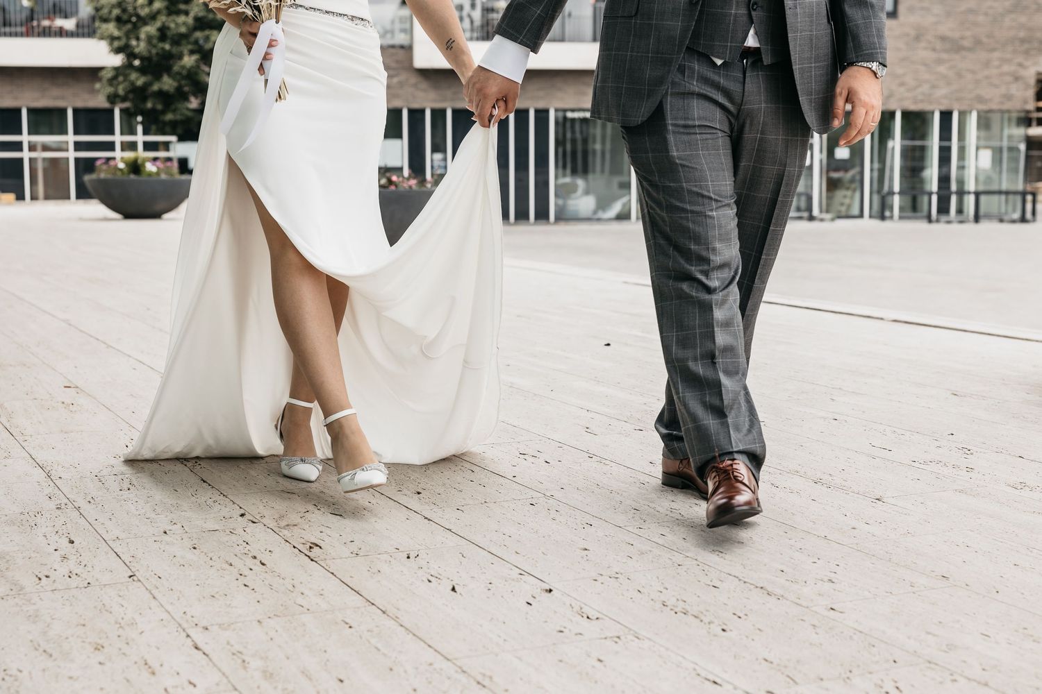 Close-up of bride and groom walking hand in hand, bride wearing white heels and flowing wedding dress.
