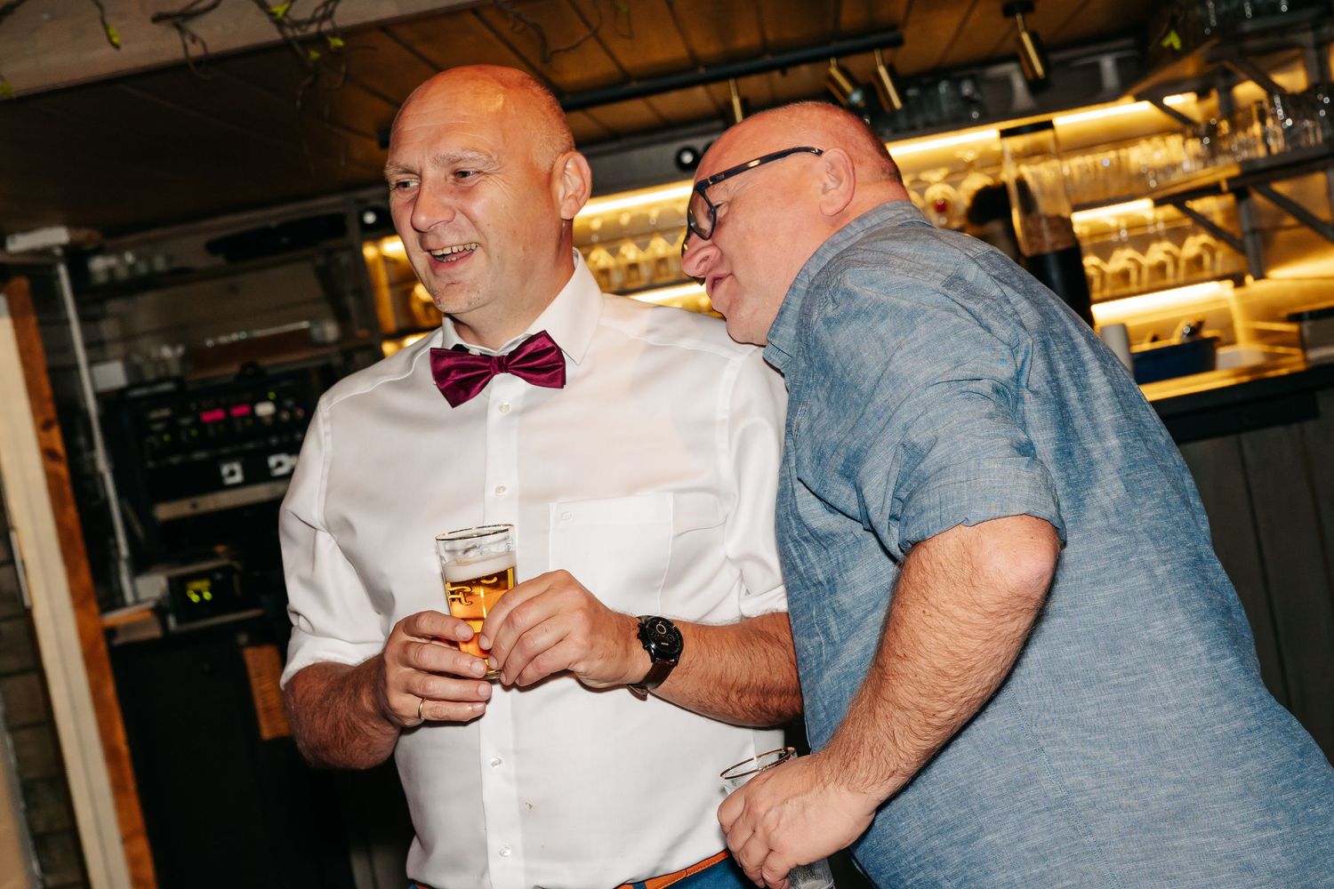 Two men laughing together while holding drinks at a wedding reception.