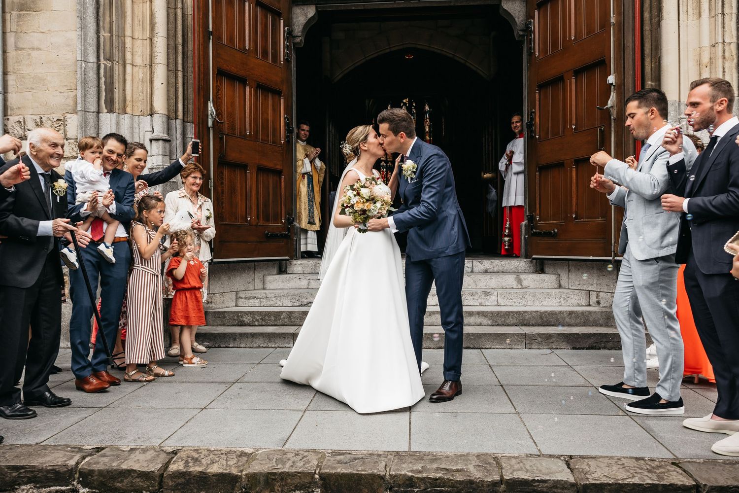 Couple kisses outside church doors as guests applaud their wedding.