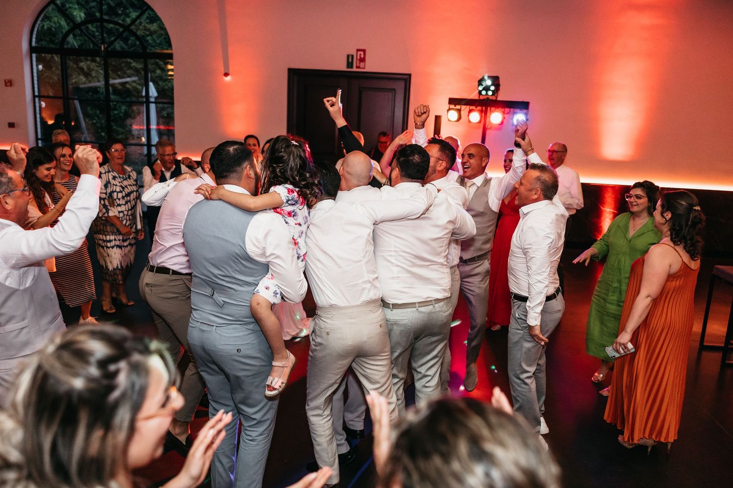 Energetic wedding guests crowding dance floor in lively celebration at indoor reception.