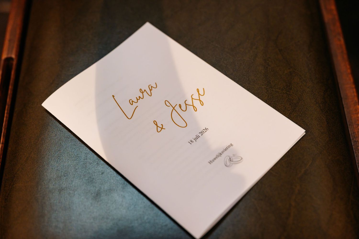 Elegant gold script wedding program booklet reading Laura and Jesse on wooden surface.