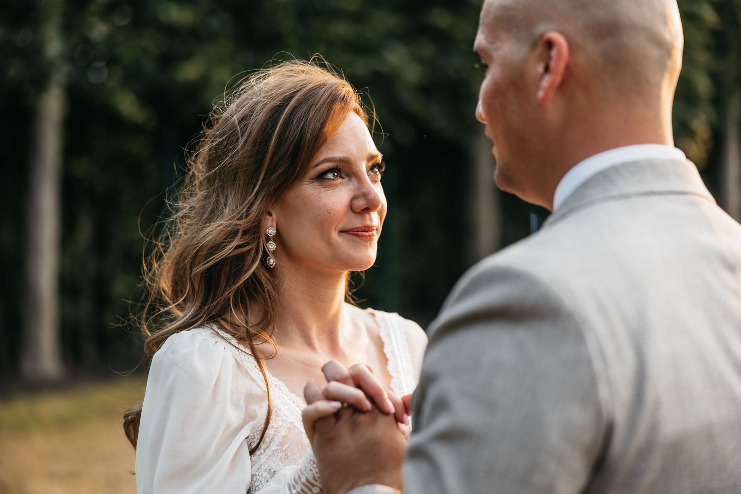 Emotional bride gazing at groom while holding hands during an intimate outdoor wedding ceremony.