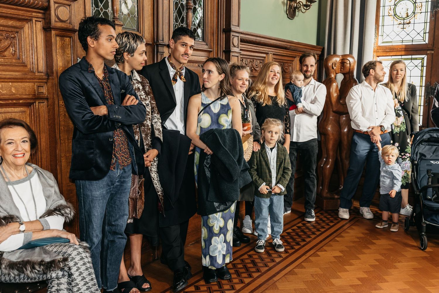 Group of wedding guests including children standing together in a grand wood-paneled ceremony room.