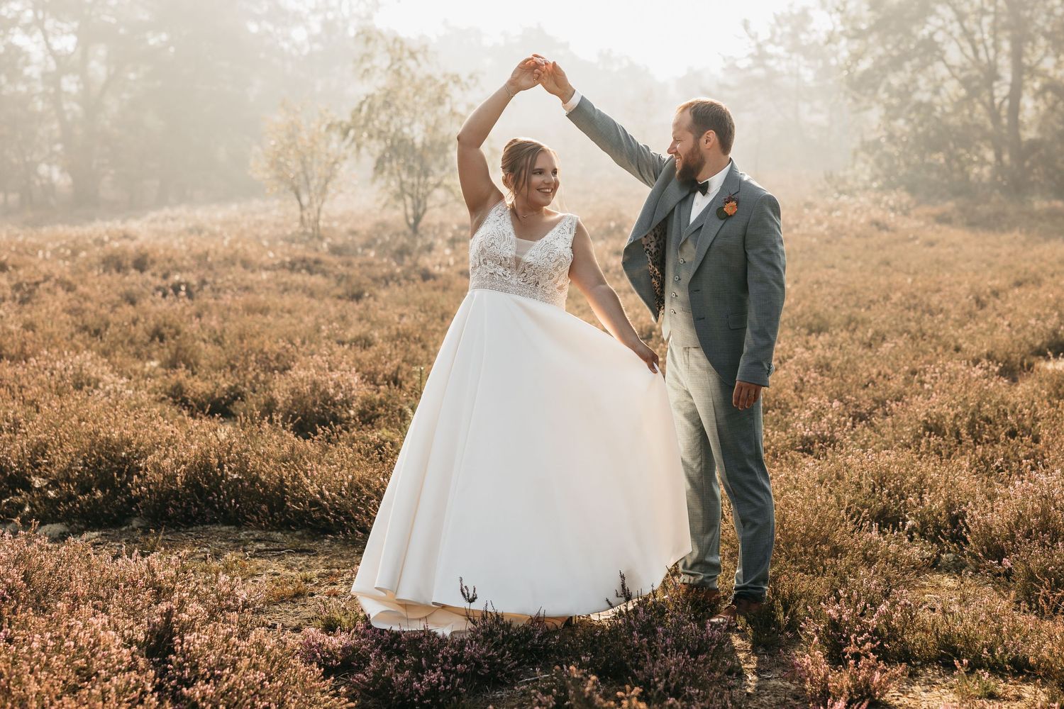 Bride and groom dancing joyfully in misty heather field, groom raising bride's hand in a spin.