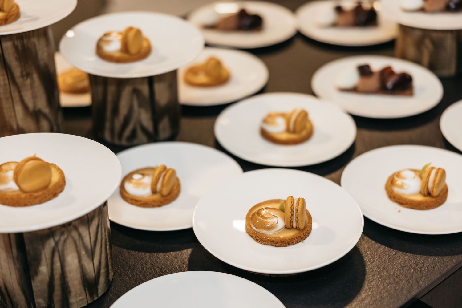 Elegant wedding dessert plates with caramel pastries displayed on wooden pedestals at reception.