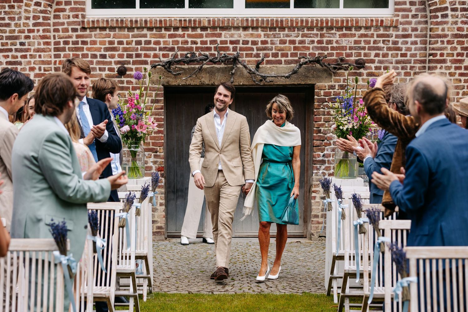 Bride and groom walking down outdoor aisle between rows of white chairs and guests.