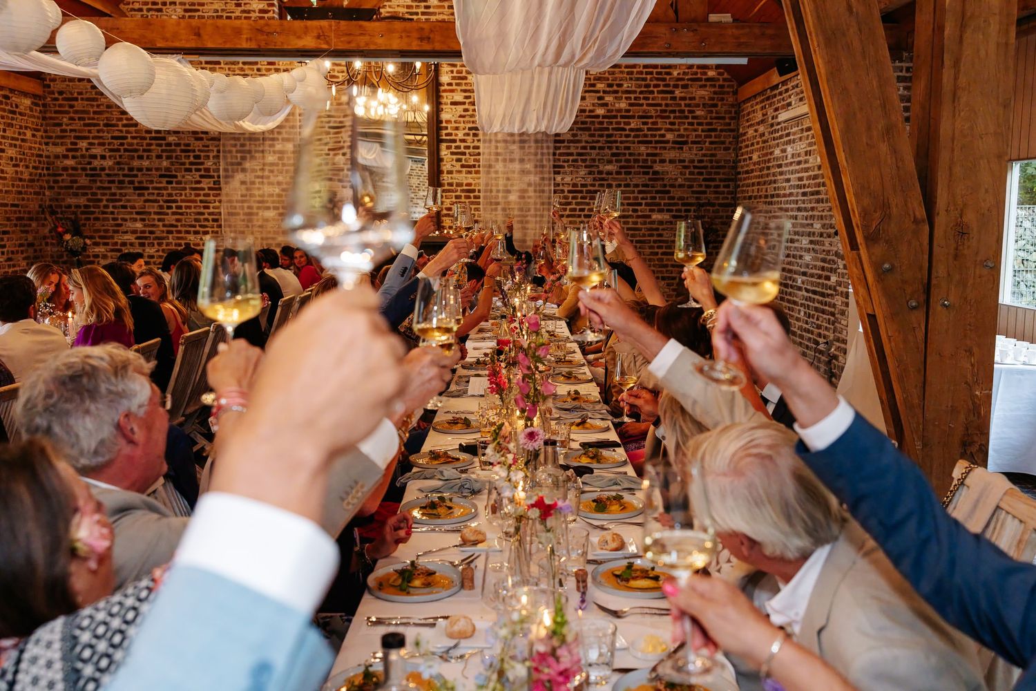 Wedding guests raising glasses in a toast at elegant rustic barn reception dinner.
