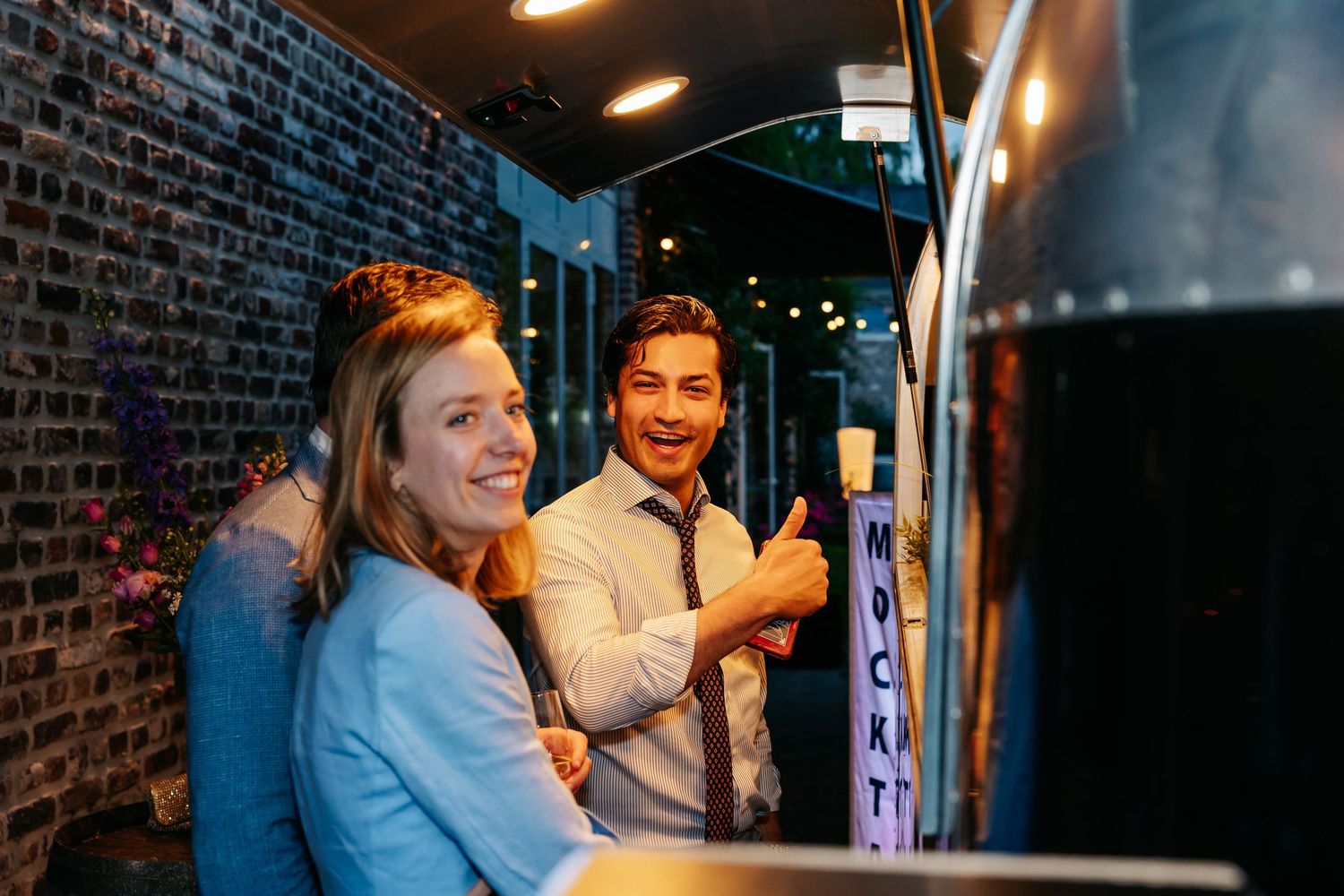 Smiling couple giving thumbs up at a food truck during wedding reception.