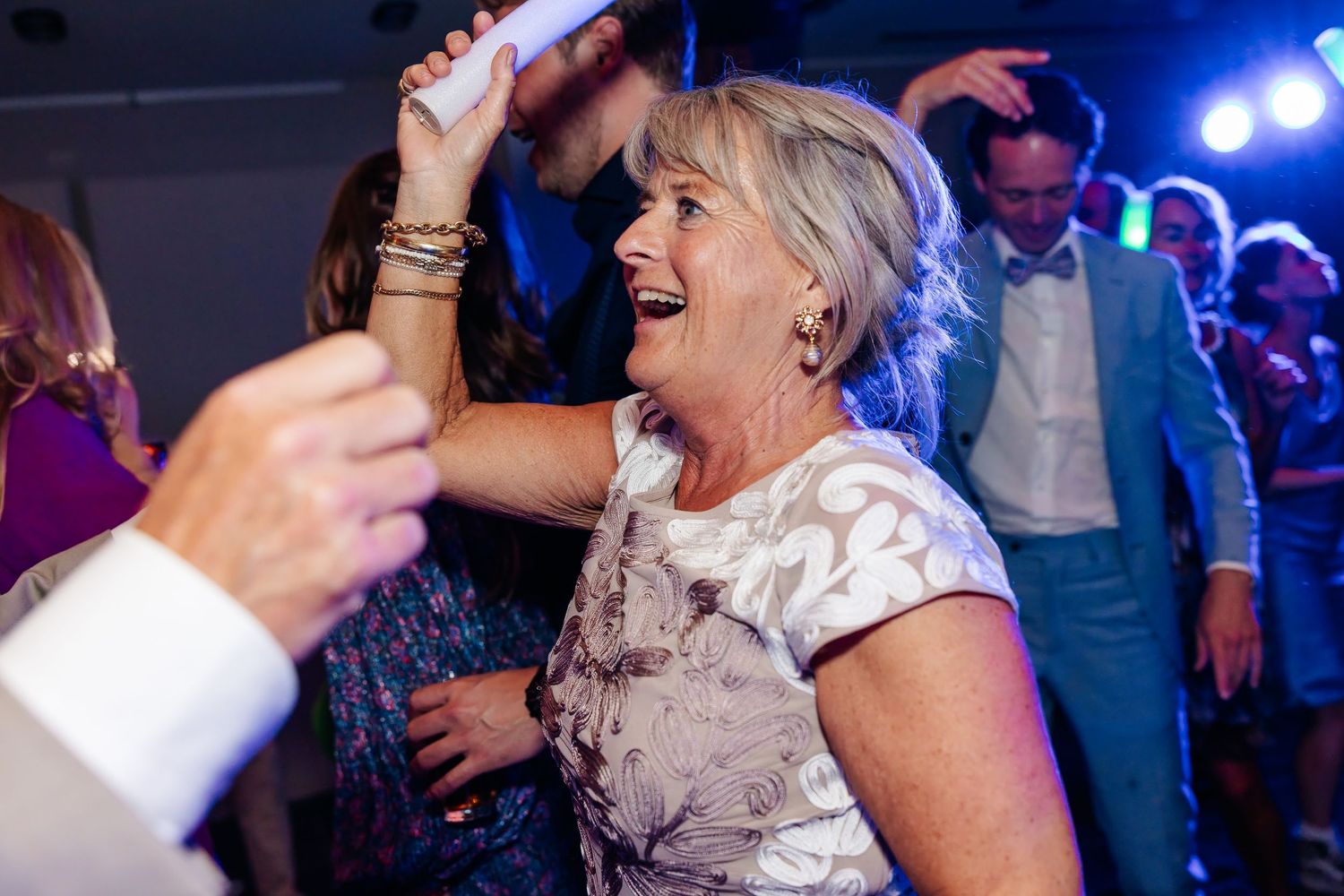 Joyful older woman laughing and dancing at a wedding reception under blue party lights.