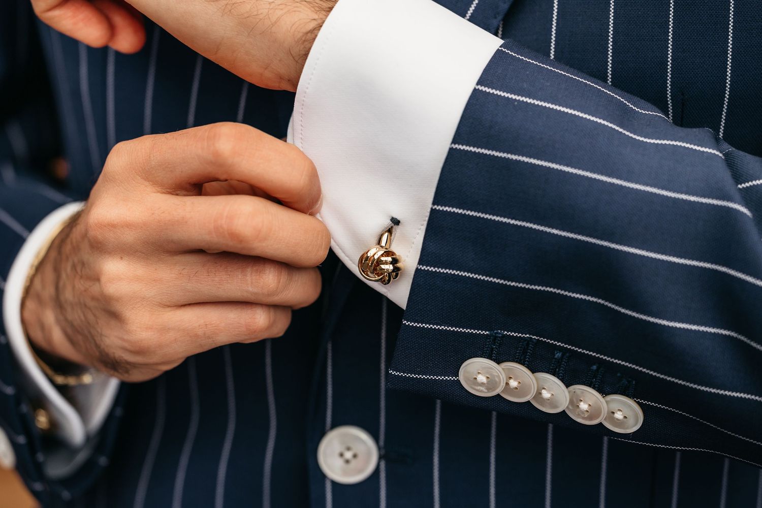 Close-up of gold anchor cufflink on white dress shirt with navy pinstripe wedding suit sleeve.