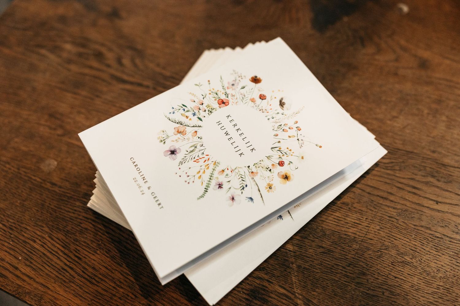 Stack of elegant floral-designed wedding ceremony programs on wooden table for church wedding.
