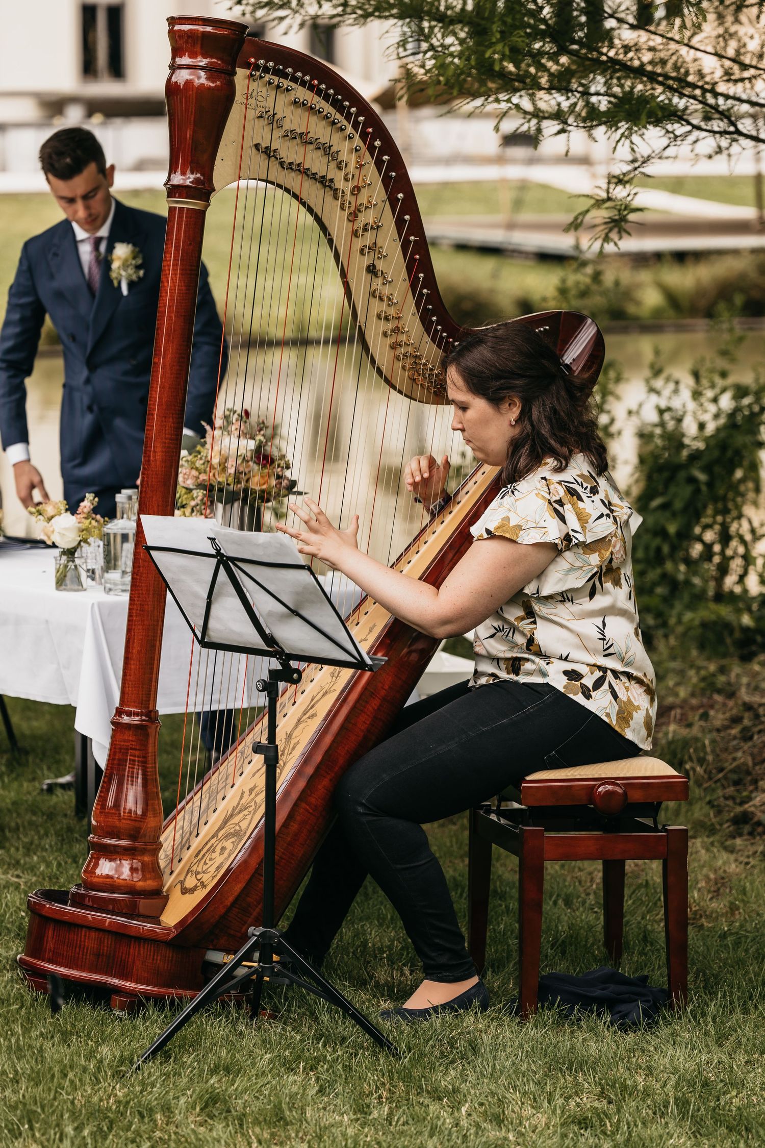 Female harpist performs live music during an outdoor garden wedding ceremony on a sunny day.