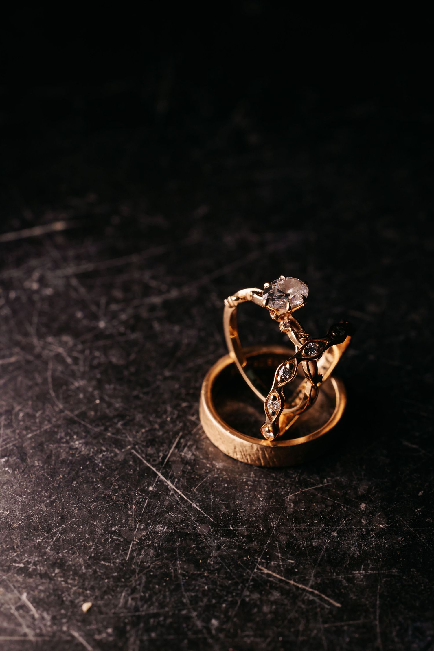 Elegant gold diamond engagement ring and wedding band displayed on a dark textured surface.