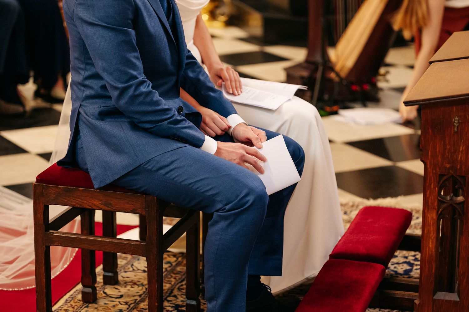 Close-up of bride and groom holding ceremony booklets while seated during church wedding.