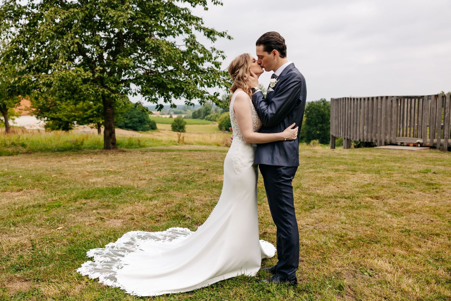 Bride in a lace wedding gown with long train and groom in navy suit share an intimate moment outdoors.