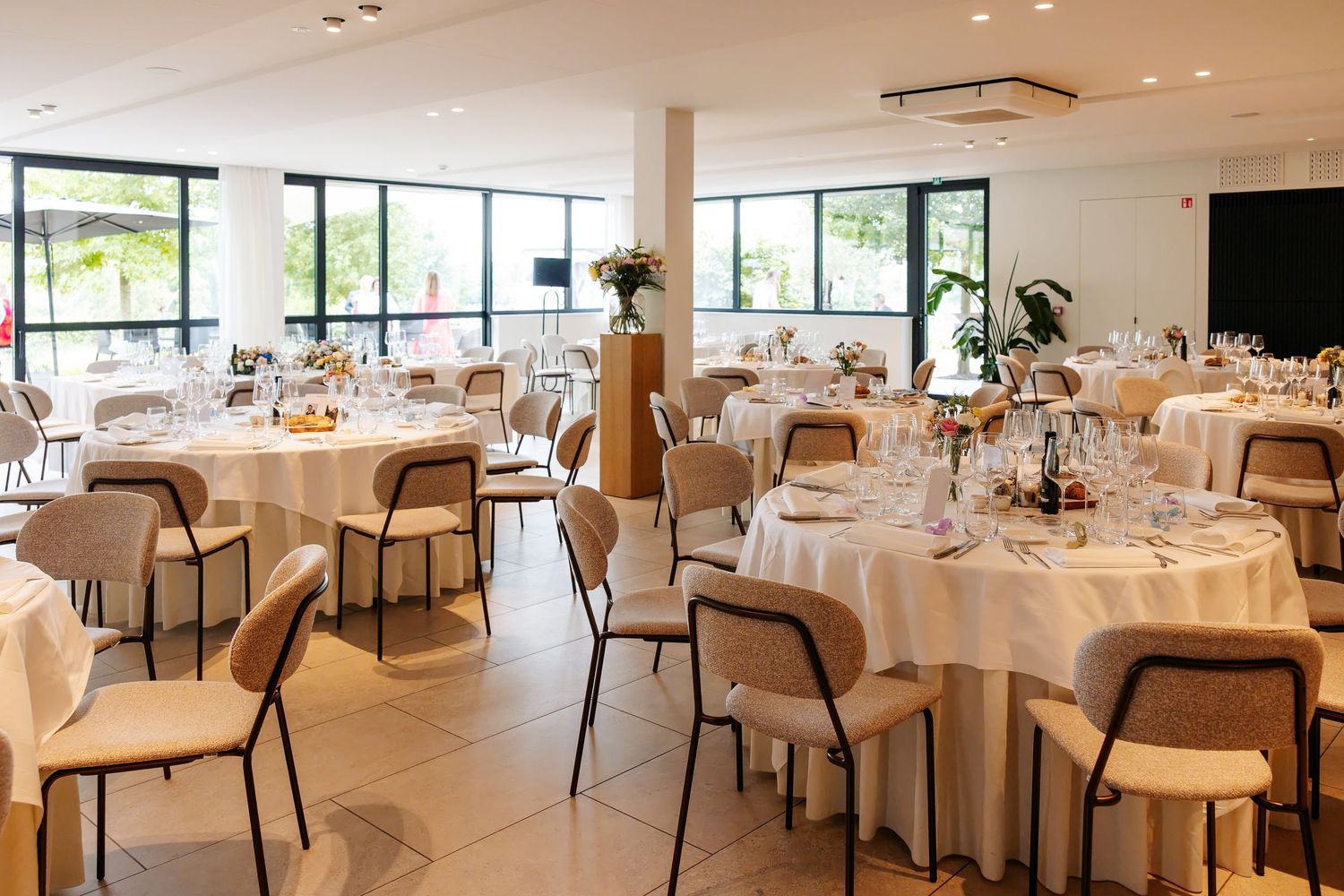 Bright wedding reception venue with round tables set in white linens, crystal glasses, and floral centerpieces.