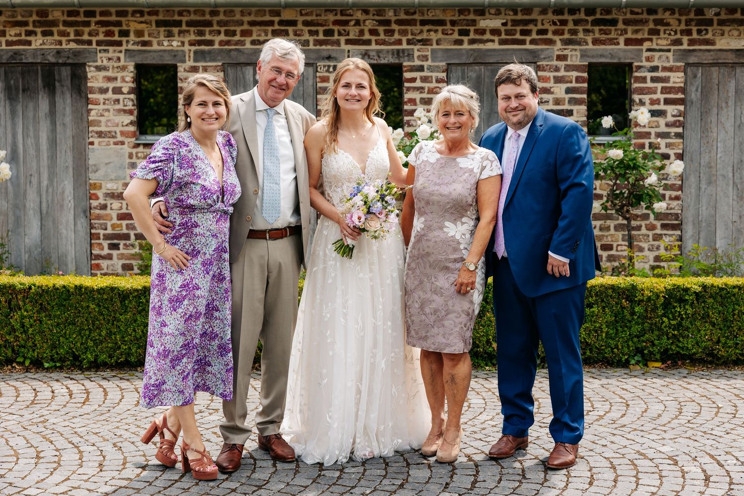 Bride and groom posing with family of four on cobblestone wedding venue.