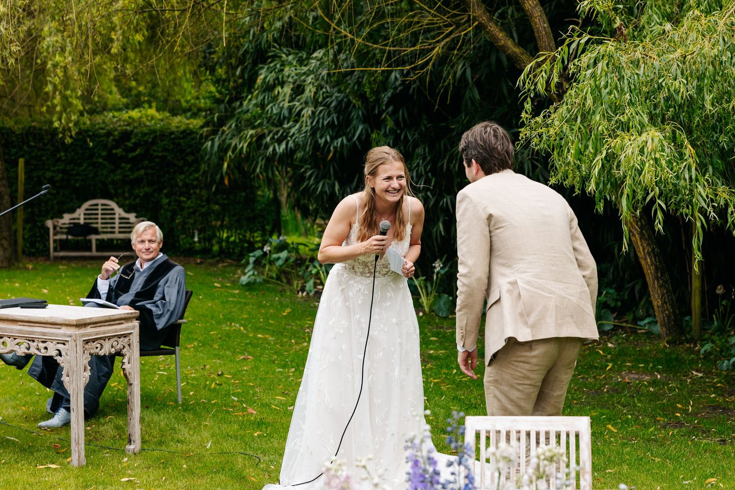 Bride laughing with groom during outdoor wedding ceremony in lush green garden.