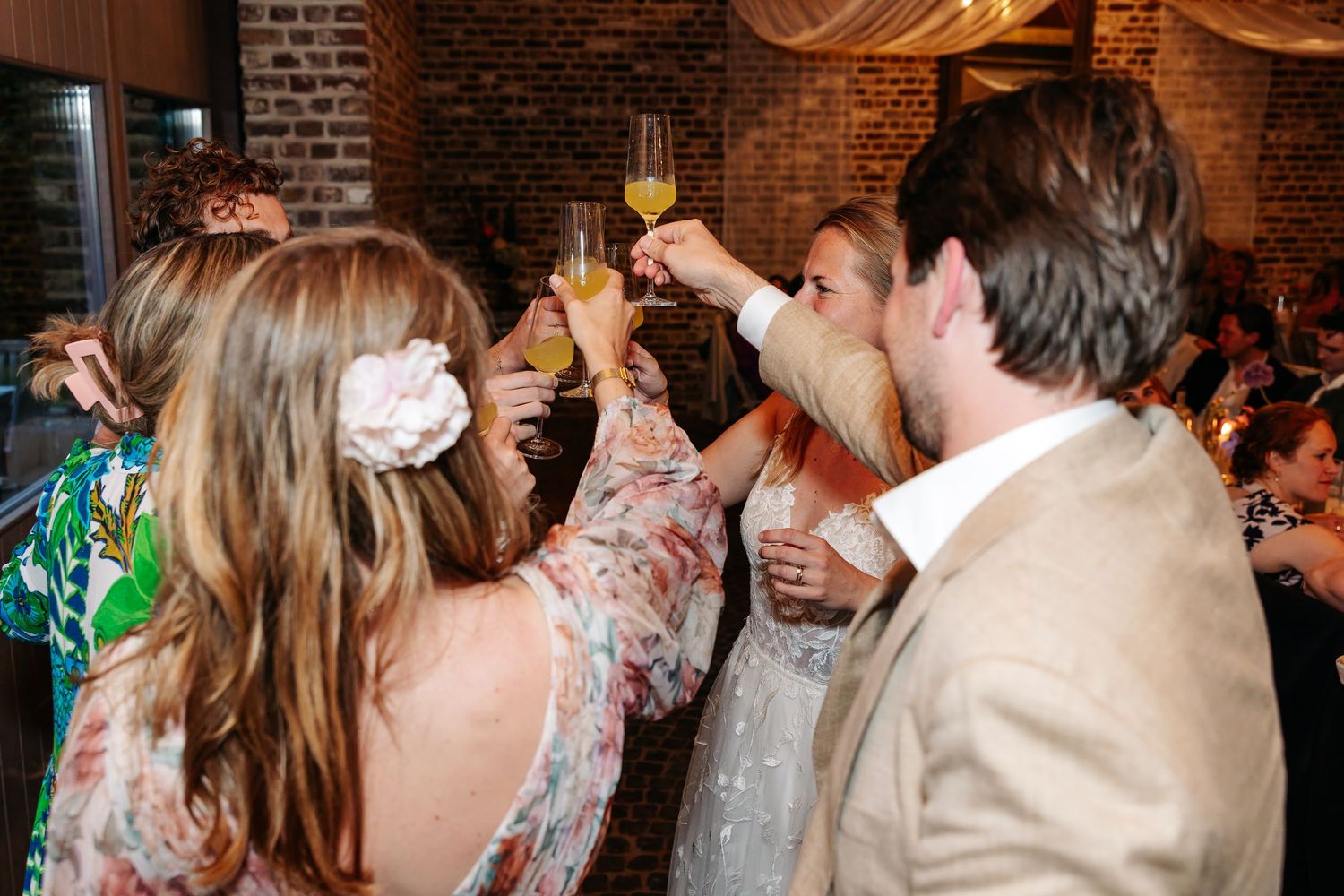 Wedding guests raising champagne glasses in a celebratory toast at a festive indoor reception.