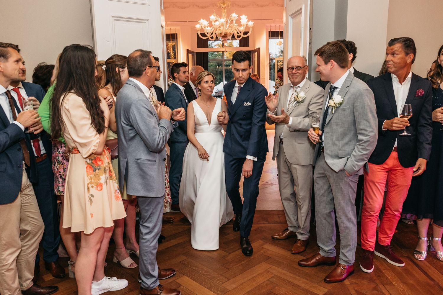 Bride and groom walking through cheering guests in elegant wedding venue hallway.