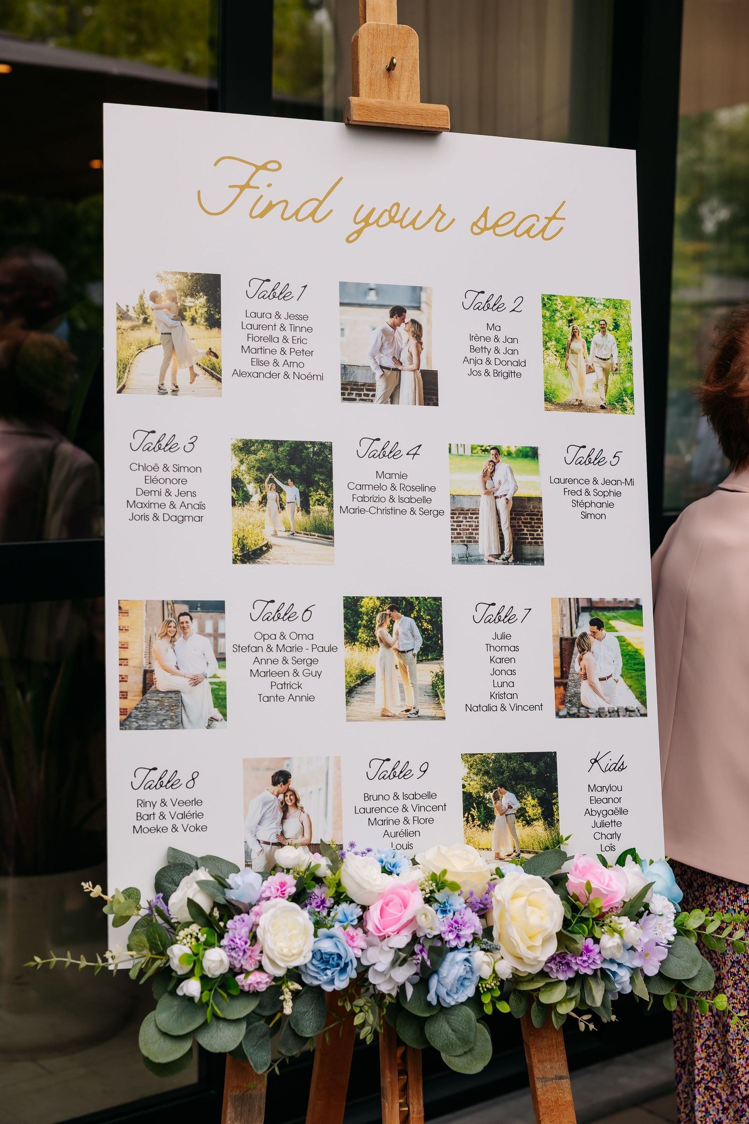 Elegant wedding seating chart on easel with couple photos and floral arrangement.