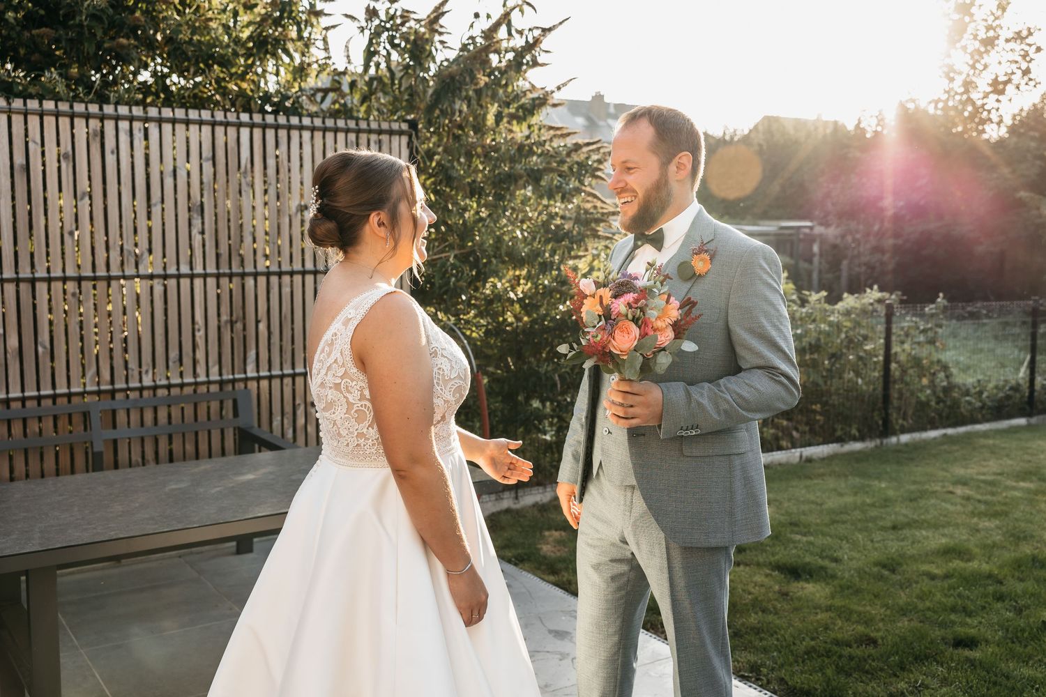 Bride and groom share a joyful first look moment outdoors with beautiful golden sunset light behind them.
