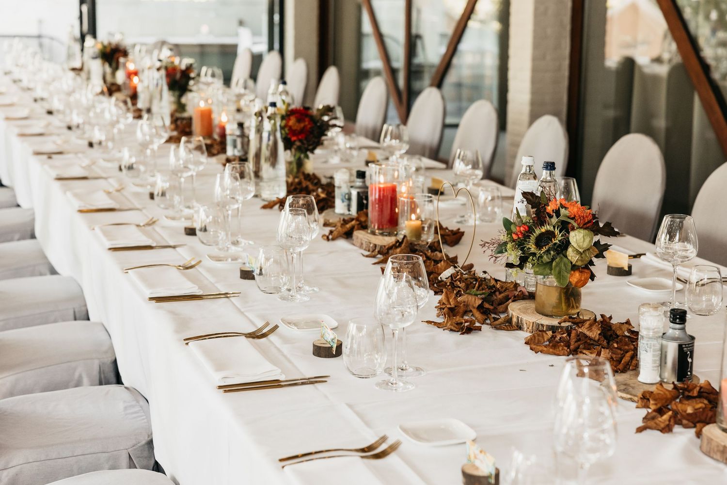 Wedding reception table with autumn floral decor, candles, and white linens.