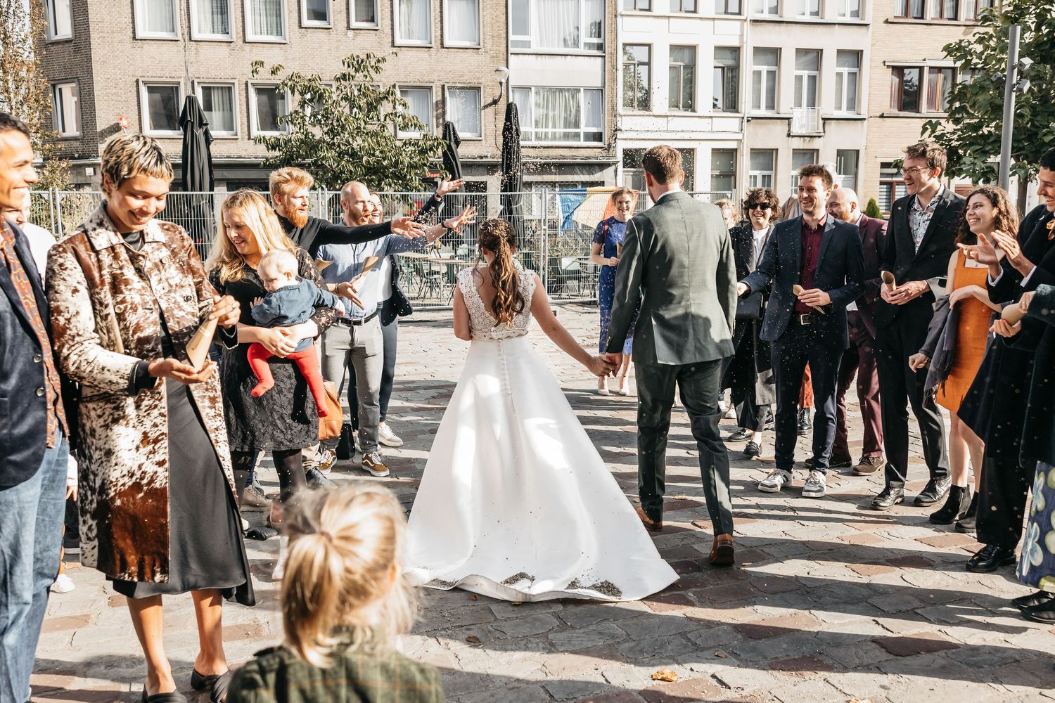 Bride and groom walk through cheering guests in bright sunny outdoor wedding celebration square.