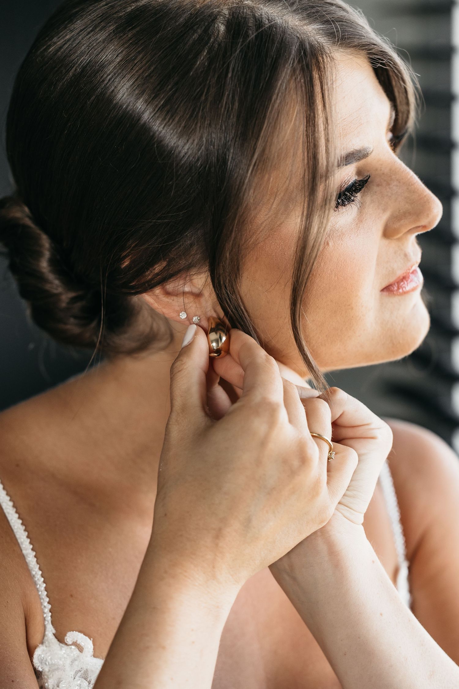 Profile view of bride smiling as gold earrings are placed in her ears.