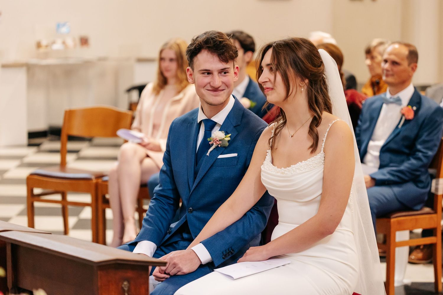 Smiling bride and groom share a joyful moment while seated during church ceremony.