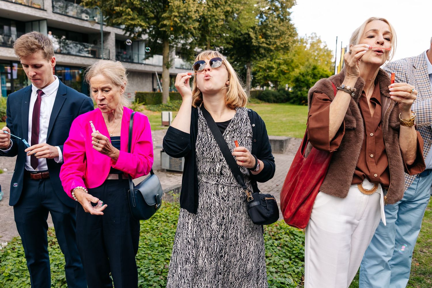 Wedding guests blowing bubbles outdoors, women in colorful dresses enjoying a celebration.