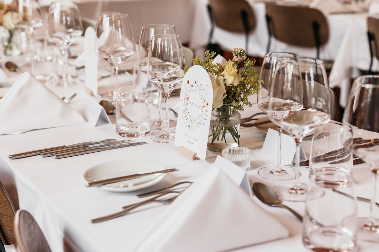 Elegant wedding reception table setting with white linens, crystal glasses, and floral centerpieces.