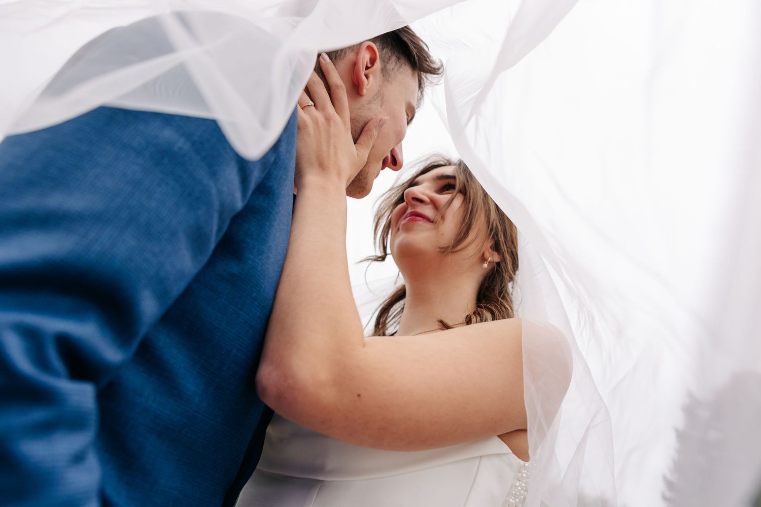Romantic moment of bride and groom sharing an intimate look beneath a flowing white veil.