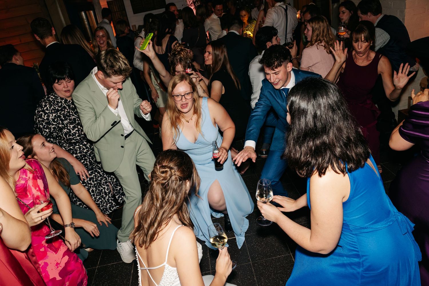 Guests dancing energetically on a crowded wedding reception dance floor.