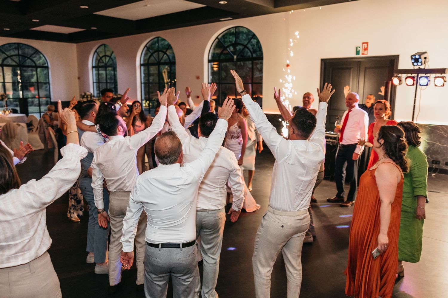 Excited wedding guests raising hands together on dance floor during festive reception party.