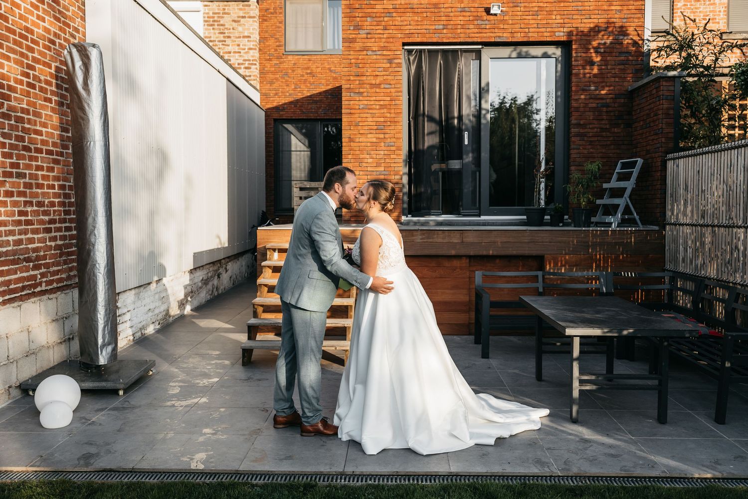 Bride and groom share a kiss in a sunny outdoor courtyard setting.