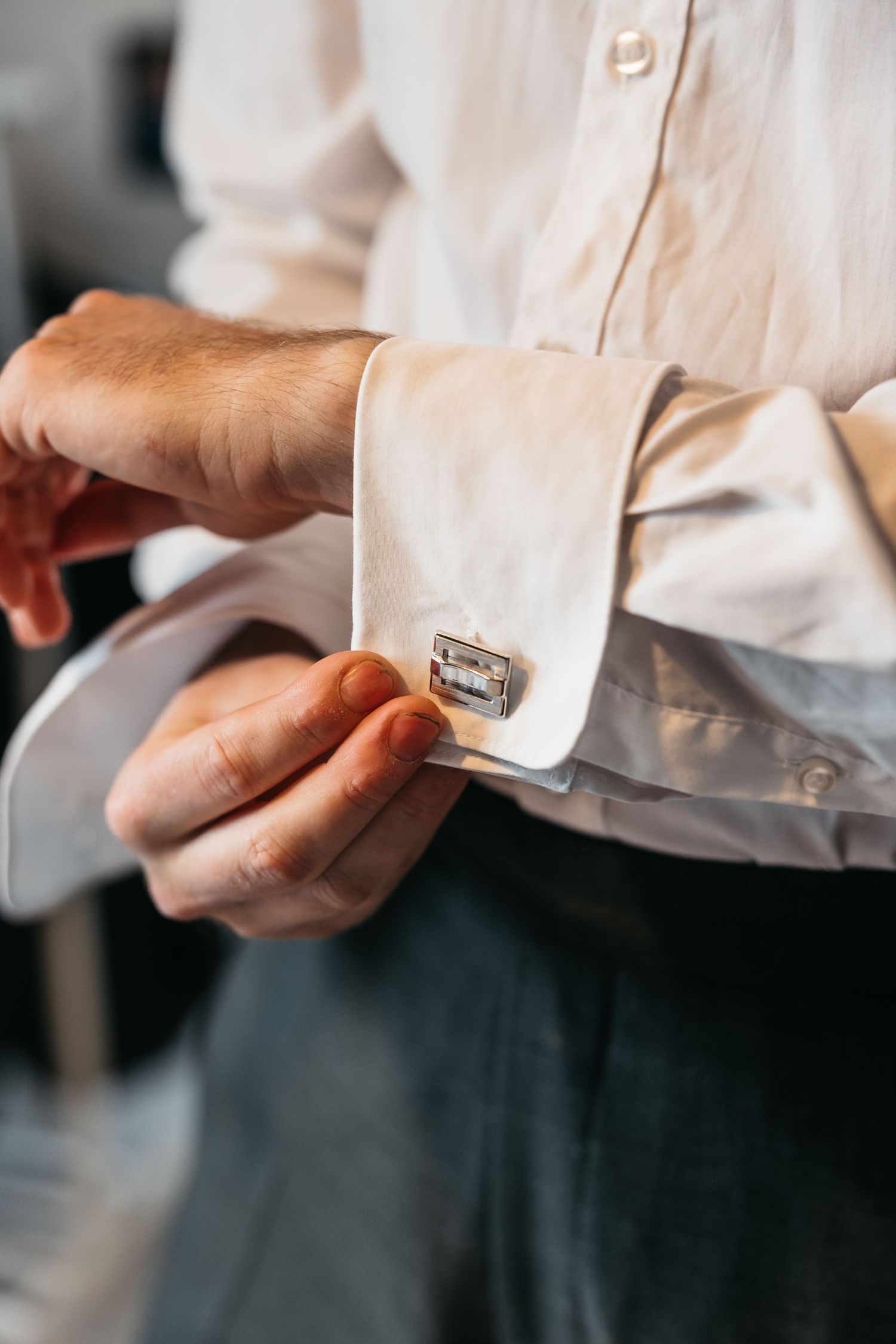Groom fastening silver cufflinks on white dress shirt sleeves before wedding ceremony.
