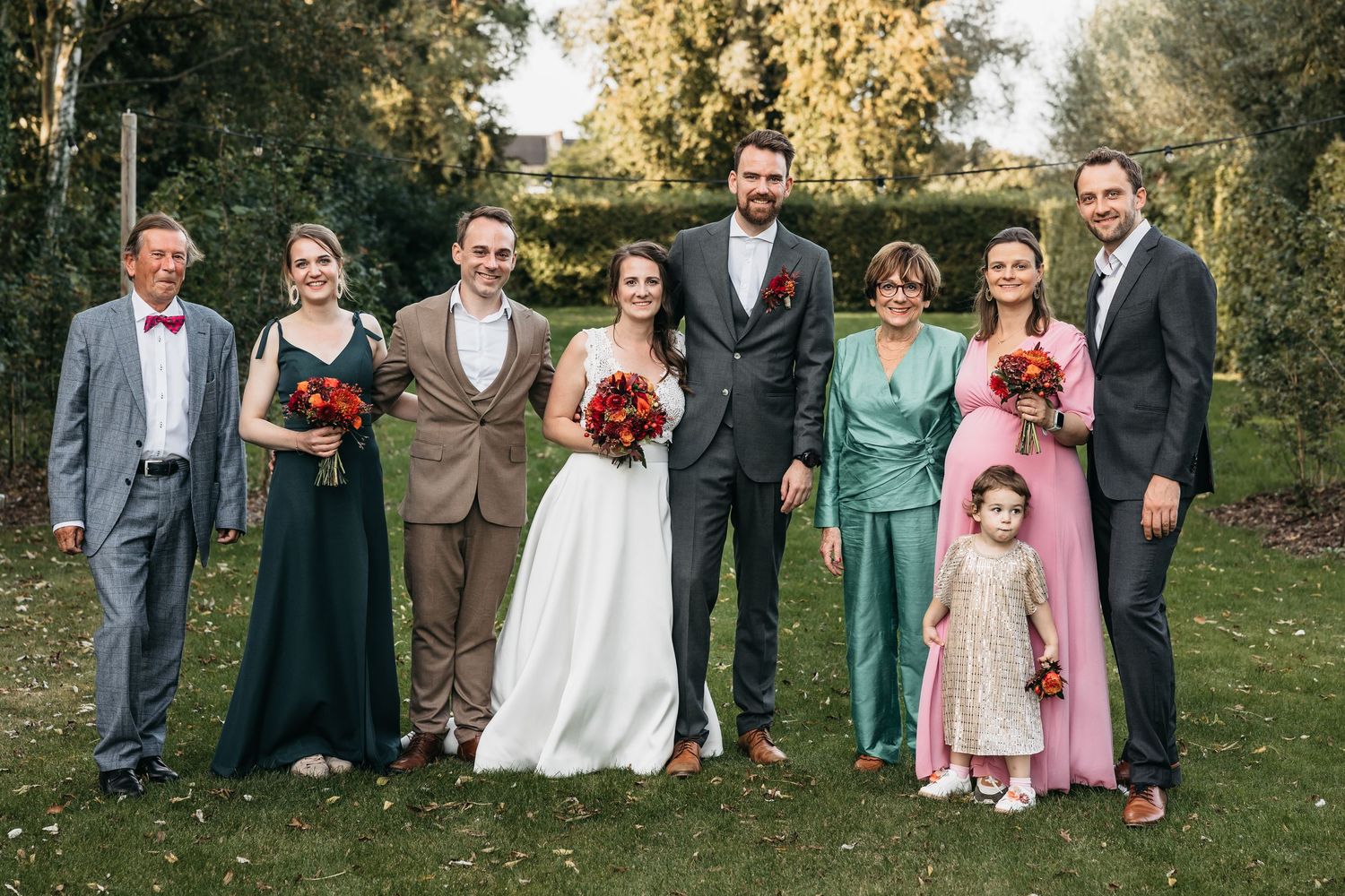Wedding family portrait with bride groom and seven relatives including flower girl on green lawn outdoors.