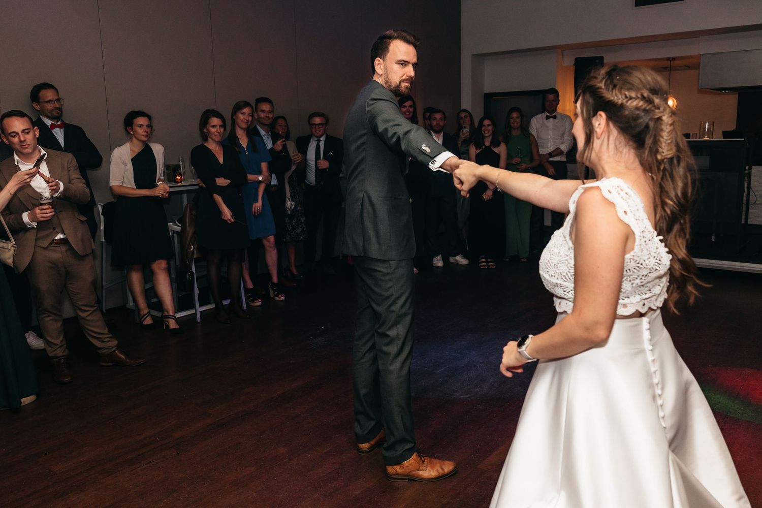 Groom leads bride by the hand across the dance floor at elegant wedding reception.