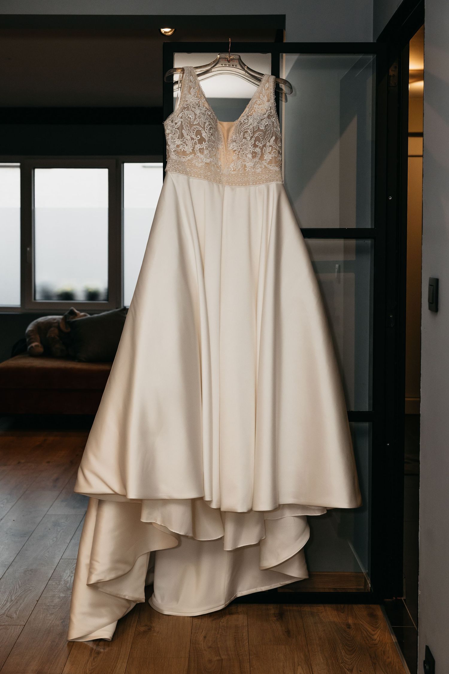 Elegant ivory A-line wedding dress with lace bodice hanging on a hanger in a modern room.