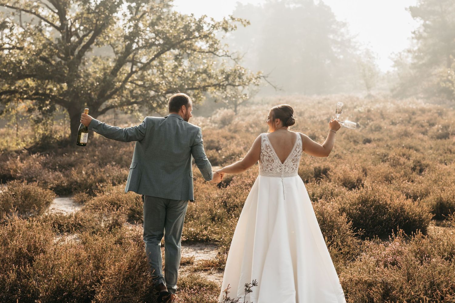 Bride and groom walking away hand in hand through misty heather field toward a scenic tree.