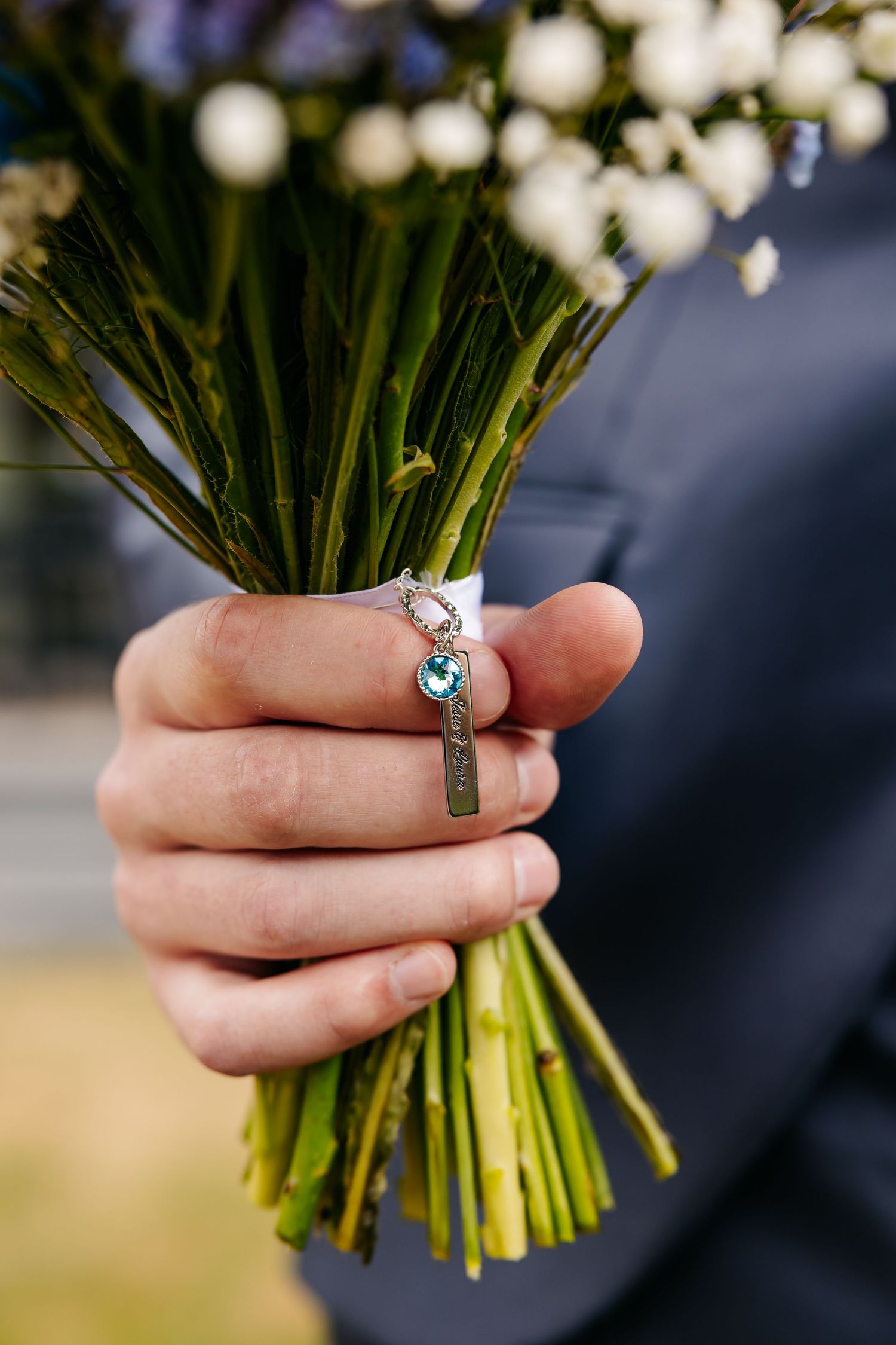 Close-up of groom holding bridal bouquet with decorative charm pendant attached to stems.