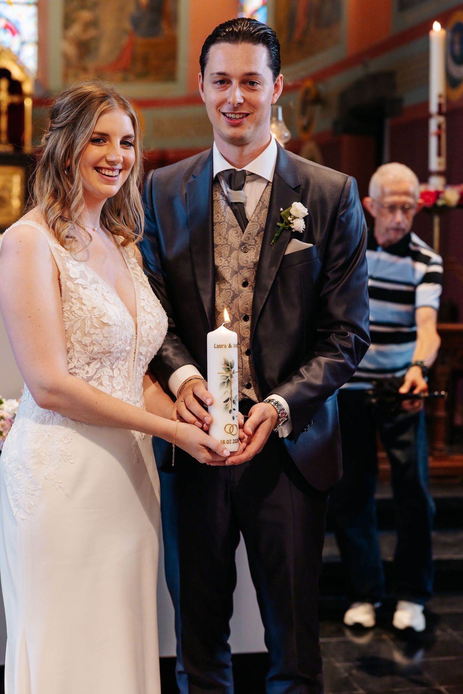 Smiling bride and groom hold unity candle together during church wedding ceremony.